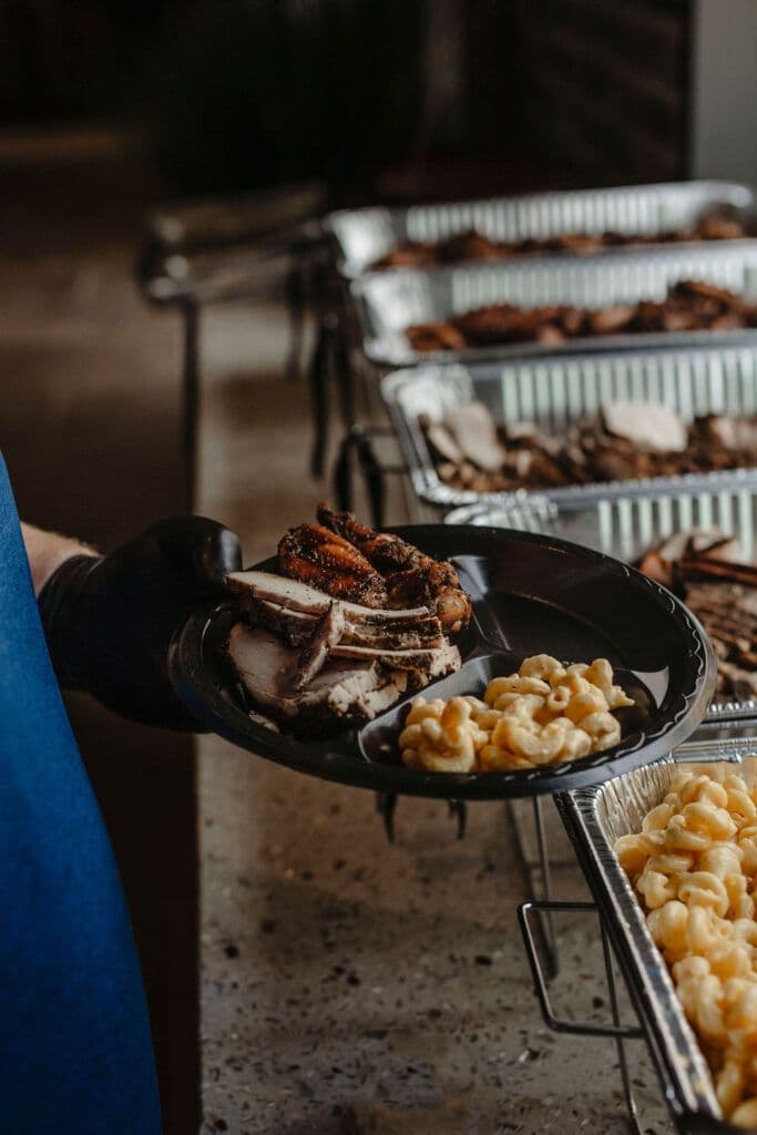 A catering plate of sliced brisket and mac & cheese with chafing trays behind