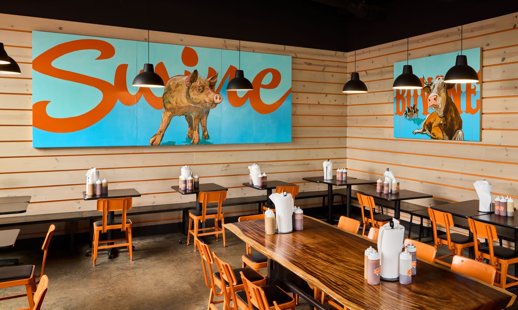 The Bearded Pig dining room with wood tables, orange chairs and the Swine mural