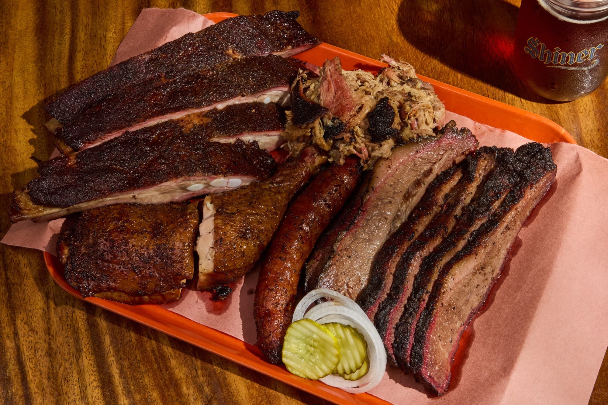 An overhead barbecue sampler tray with brisket, ribs, pulled pork and sausage